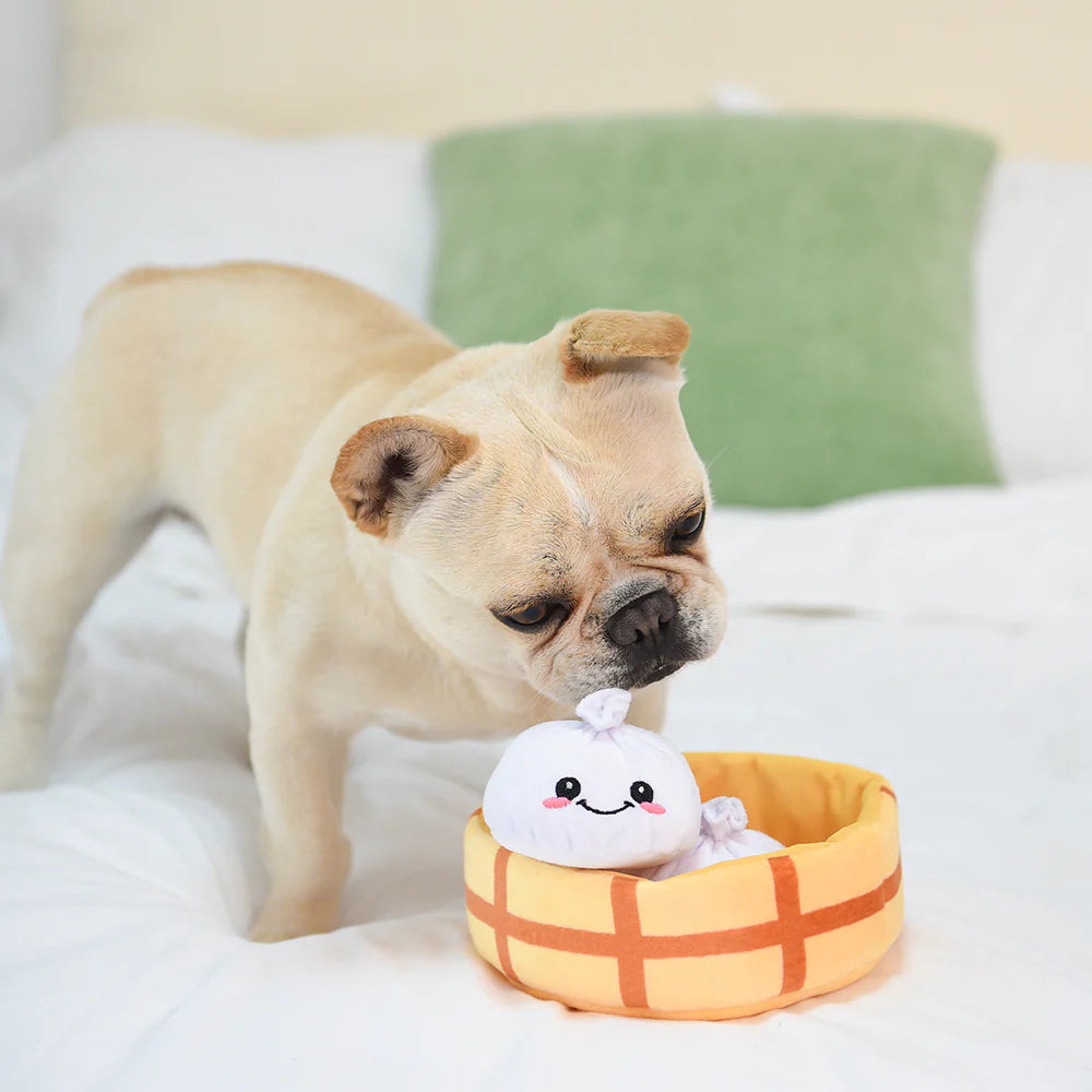 Curious dog playing with the hugsmart dumpling plush toy set on a white bed